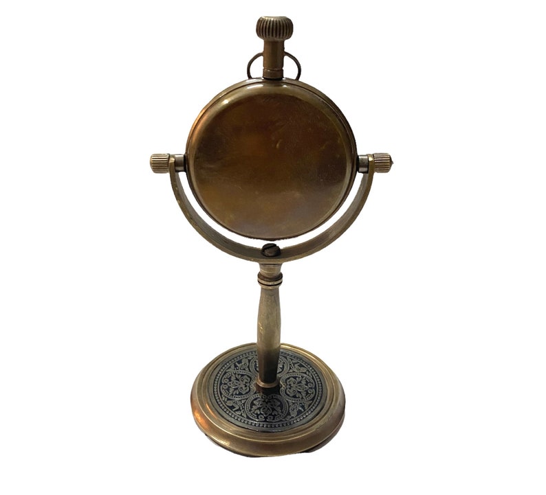 May include: A brass antique-style clock with a round face and a decorative stand. The clock has a black and gold design on the base.