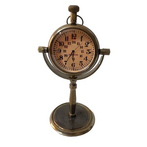 May include: A brass desk clock with a round face and a stand. The clock face has Roman numerals and a 24-hour time scale. The clock is on a stand with a round base.