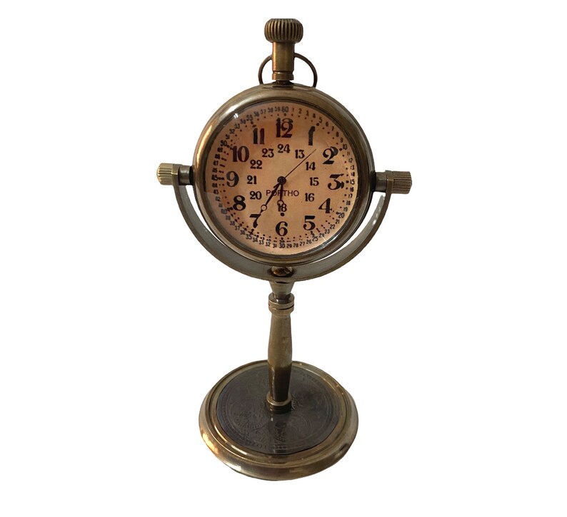 May include: A brass desk clock with a round face and a stand. The clock face has Roman numerals and a 24-hour time scale. The clock is on a stand with a round base.