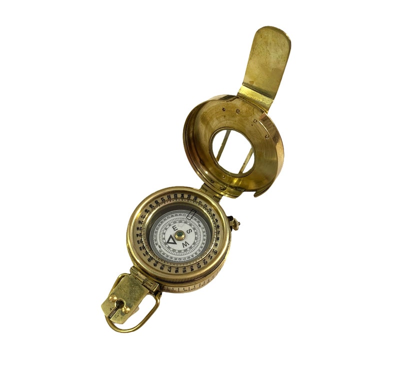 K&ouml;nnte beinhalten: Ein Kompass aus Messing mit einem Klappdeckel und einem wei&szlig;en Zifferblatt mit schwarzen Markierungen. Der Kompass hat eine Nadel, die nach Norden, S&uuml;den, Osten und Westen zeigt. Der Kompass ist ein Vintage-Artikel und hat einen abgenutzten Look.