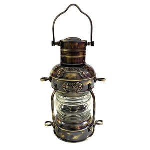 Op de afbeelding: Een antieke messing ankerlamp met een heldere glazen bol. De lamp heeft een handvat om te dragen en is voorzien van de tekst "ANCHORLAMP" en "LEEDS BURTON SOUTHAMPTON". De lamp heeft een vintage, nautische uitstraling.