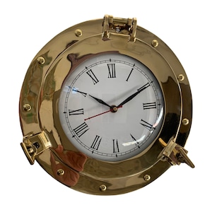 May include: A gold-toned brass clock with Roman numeral markings on a white face. The clock is set in a round brass frame that resembles a ship's porthole.