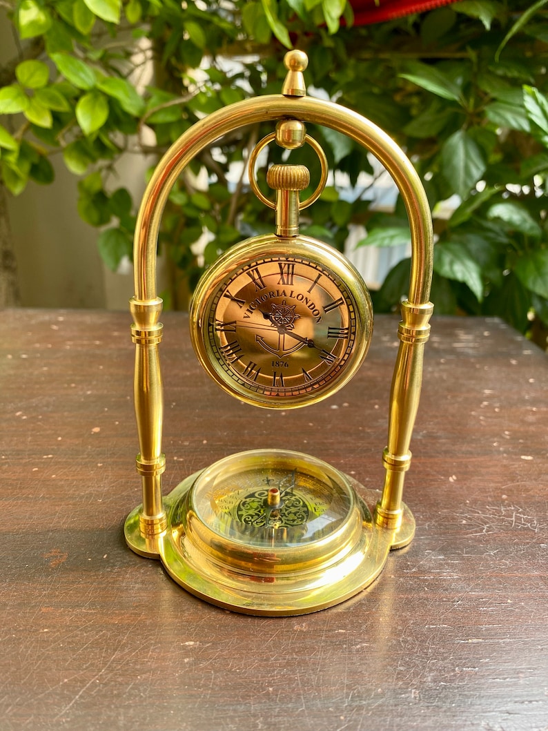 May include: A gold-toned pocket watch with a compass base. The watch face has Roman numerals and the words "Victoria London 1876".