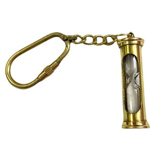 May include: A brass hourglass keychain with a clear glass tube filled with white sand. The keychain has a brass loop and chain.