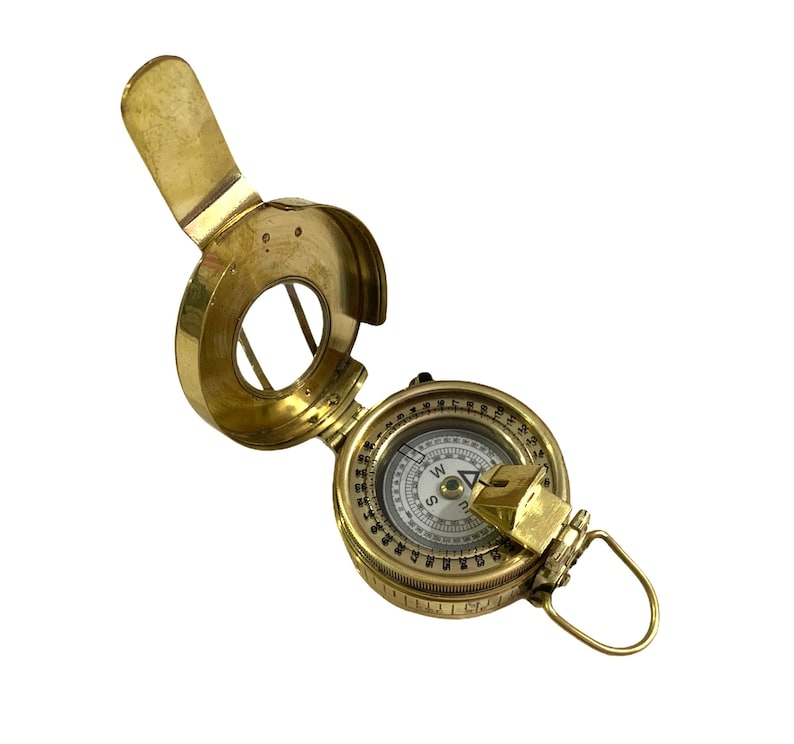 K&ouml;nnte beinhalten: Ein Kompass aus Messing mit einem klappbaren Visier. Das Kompassgesicht hat einen wei&szlig;en Hintergrund mit schwarzen Markierungen und einer roten Nadel.