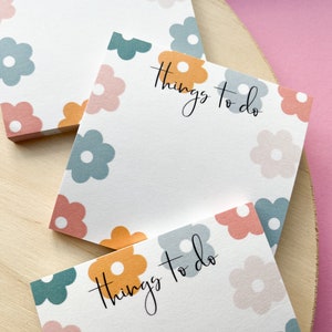 May include: Three white sticky note pads with a floral pattern in shades of blue, pink, and orange. The text "Things to do" is written in black cursive on each pad.