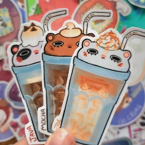 Könnte beinhalten: Drei illustrierte Aufkleber von Eiskaffee-Getränken mit Schlagsahne und Strohhalmen. Die Getränke sind mit "Java", "Mocha" und "Joe" beschriftet.