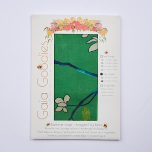 Puede incluir: Un paquete de bolsas de cera de abejas Gaia Goodies. El paquete presenta un diseño floral verde con flores blancas y detalles azules. El texto en el paquete incluye "beeswax bags - bagged by bees" y detalles del producto. El paquete mide aproximadamente 25 cm por 20 cm.