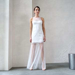 May include: A white sleeveless dress with a sheer tulle overlay. The dress has a fitted bodice and a flowing skirt.