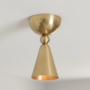May include: A gold-colored, modern ceiling light fixture. The fixture has a bowl-shaped top, a spherical mid-section, and a conical bottom. The interior of the cone is illuminated, creating a warm glow. The light is mounted on a white ceiling.