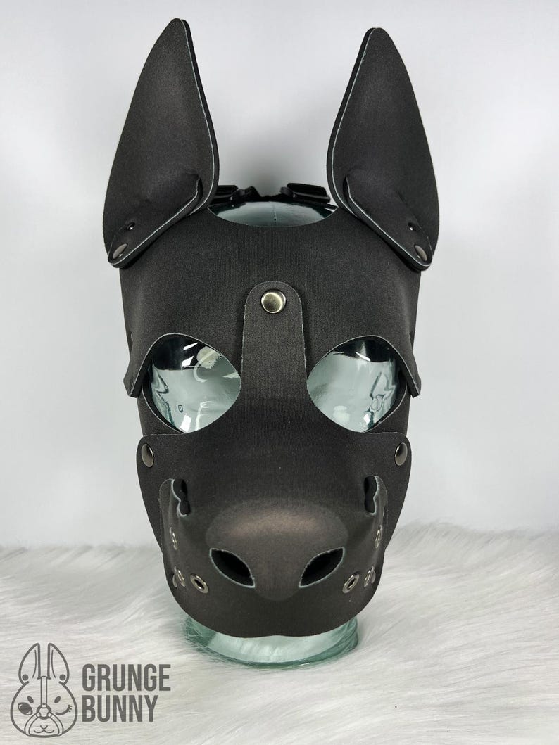 May include: Black leather pup mask with large, upright ears, eye openings, and a muzzle with air holes. The mask is secured with rivets and straps. The Grunge Bunny logo is visible at the bottom left.