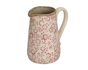 Op de afbeelding: Een witte keramische kan met een roze bloemenpatroon. De kan heeft een handvat en een brede opening.
