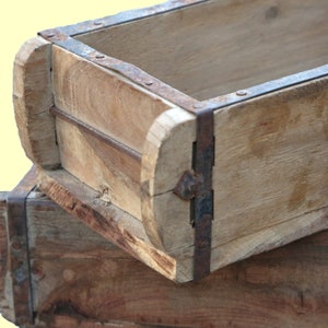 Könnte beinhalten: Zwei Holzkisten mit Metallbändern. Die Kisten sind übereinander gestapelt. Die obere Kiste ist leer und die untere Kiste ist teilweise sichtbar.