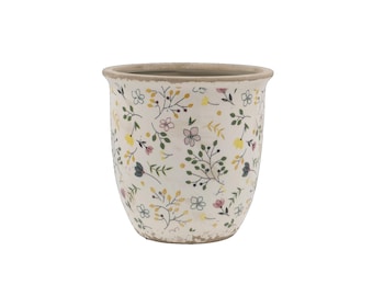 Puede incluir: Una maceta de cerámica color crema con un estampado floral. La maceta presenta pequeñas flores amarillas, rosas y moradas, junto con hojas verdes. El borde tiene un acabado marrón claro desgastado.