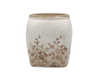 May include: A white ceramic pot with a slightly distressed appearance. The pot features a brown floral pattern around the base and a light brown rim. The design gives it a vintage or antique aesthetic.