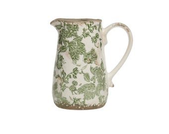 May include: A white ceramic pitcher with a green floral pattern. The pitcher has a handle and a spout.