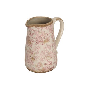 Könnte beinhalten: Ein weißer Keramikkrug mit rotem Blumenmuster. Der Krug hat einen gebogenen Griff und ein leichtes Vintage-Aussehen. Der Rand und der Boden haben eine braune Umrandung. Ein dekoratives Stück für Küche oder Esszimmer.