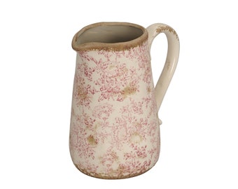 Puede incluir: Una jarra de cerámica blanca con un estampado floral rojo. La jarra tiene un asa curva y una apariencia vintage ligeramente desgastada. El borde y la base tienen un ribete marrón. Una pieza decorativa para la cocina o el comedor.