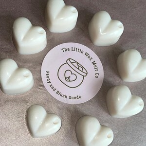 May include: Eight heart-shaped wax melts in white, arranged in a circle on a light brown surface. A pink circle label in the center reads "The Little Wax Melt Co. Peony and Blush Suede."