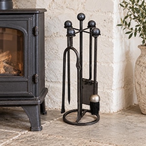 May include: A black metal fireplace tool set featuring a circular base and a central stand with four arms topped by spherical finials. The set includes a poker, a shovel, and a brush with black bristles, all suspended from the central stand.