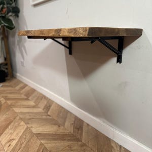 K&ouml;nnte beinhalten: Ein an der Wand montierter Klapptisch aus Holz mit schwarzen Metallkonsolen. Der Tisch ist aus recyceltem Holz gefertigt und hat eine rustikale Oberfl&auml;che.