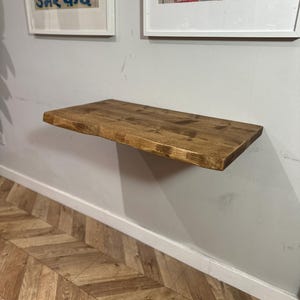 K&ouml;nnte beinhalten: Ein rustikales Holzregal mit einer nat&uuml;rlichen Holzoptik ist an einer wei&szlig;en Wand montiert. Das Regal ist etwa 76 cm lang und 15 cm breit. Das Regal ist &uuml;ber einem Holzboden mit Chevron-Muster montiert.