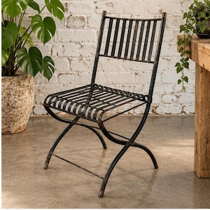 May include: A black metal folding chair featuring a slatted seat and backrest with a distressed finish. The chair has curved, crossed legs and a horizontal support bar near the base, constructed from thin metal bars throughout the frame.