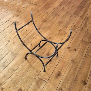 May include: Black metal log holder with a curved design. The holder is made of thin metal bars and has a simple, rustic look.