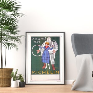 May include: A vintage Michelin advert featuring a cartoon Michelin Man holding a bicycle tyre with a woman in a blue dress standing next to him. The text on the poster reads "Enveloppe Velo Michelin".
