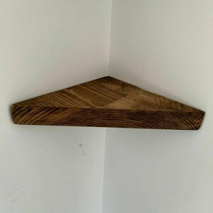 May include: A dark brown wooden corner shelf with a triangular shape. The shelf is made of natural wood with a rustic finish.