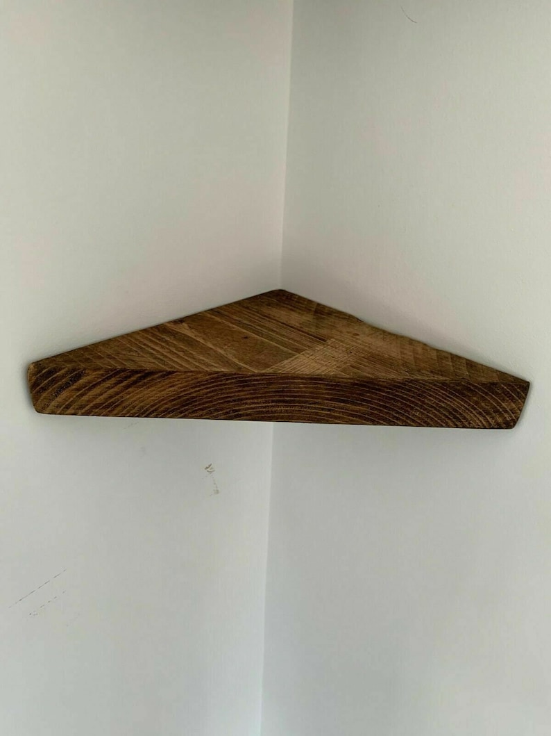 May include: A dark brown wooden corner shelf with a triangular shape. The shelf is made of natural wood with a rustic finish.