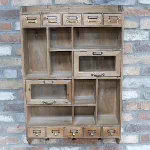 Könnte beinhalten: Ein hölzerner Wandschrank mit verschiedenen Fächern und Schubladen. Er verfügt über kleine Schubladen mit Messinggriffen oben, offene Regale und Glasfrontfächer darunter. Das Holz hat eine natürliche Oberfläche und bietet eine rustikale Ästhetik.