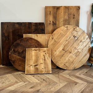 May include: A collection of wooden planks and tabletops in various shapes and sizes. The pieces include rectangular and circular designs, with natural wood grain patterns and varying shades of brown. Some pieces are dark stained, while others are light.