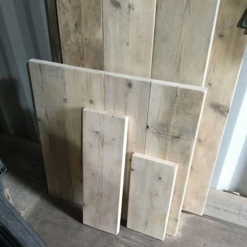 May include: Four wooden planks of varying sizes, all with a light brown color and a rough, rustic texture. The planks are stacked on top of each other, with the largest plank at the bottom and the smallest plank at the top.