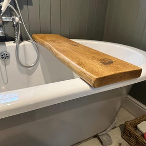 May include: A white bathtub with a wooden shelf attached to the side. The shelf is made of natural wood with a rustic finish.