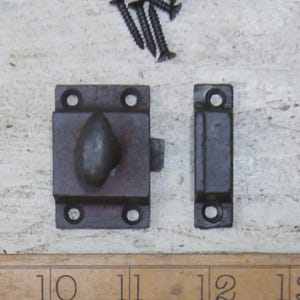 May include: A dark gray metal cabinet latch set with a rectangular base, a teardrop-shaped handle, and a matching strike plate. Includes several black screws for installation. The latch is designed for securing cabinet doors or drawers.