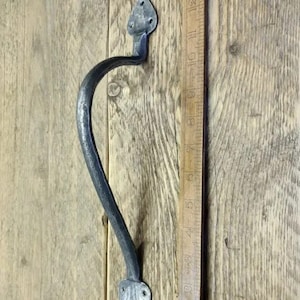 Puede incluir: Una manija de puerta de metal plateado con un diseño curvo y un extremo puntiagudo. La manija está montada en una superficie de madera.