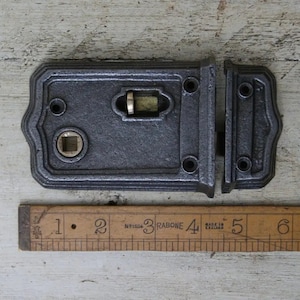 May include: A black cast iron door latch with a brass keyhole and a brass latch. The latch is 4 inches long and is shown next to a ruler.