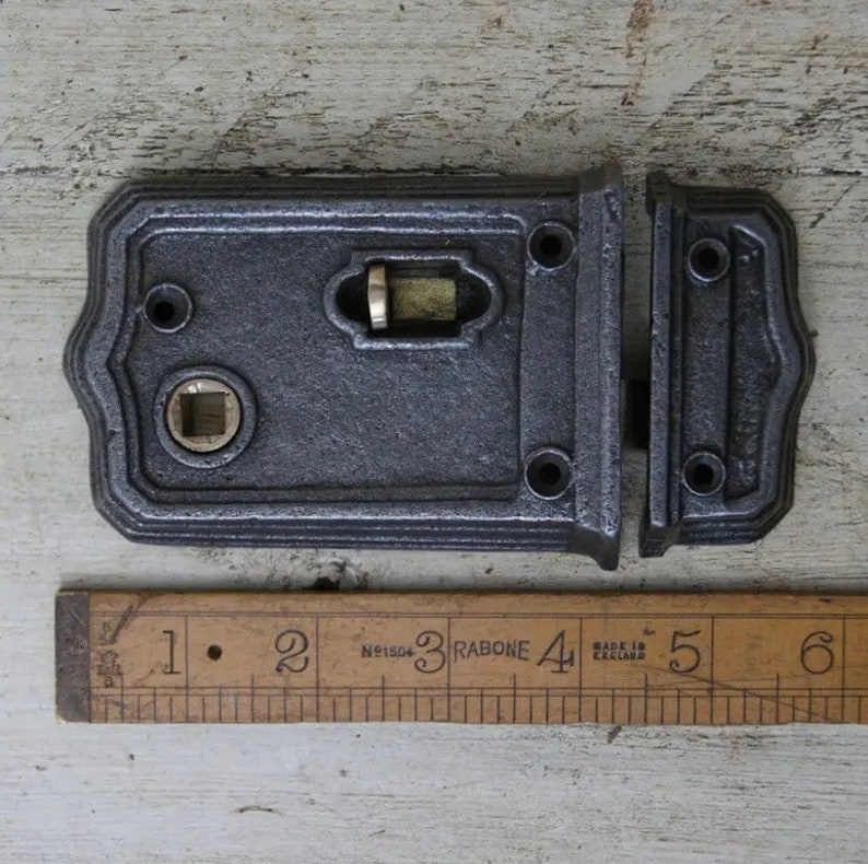 May include: A black cast iron door latch with a brass keyhole and a brass latch. The latch is 4 inches long and is shown next to a ruler.