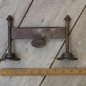 May include: A vintage metal scale with a black metal base and two upright posts. The scale has a metal bar with the inscription "Sheffield Steelworks 1930" and a circular metal tag with the inscription "1883".
