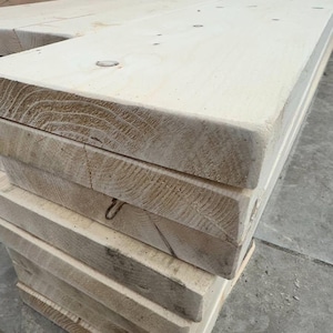 May include: A stack of unfinished, light-colored wooden planks. The planks are stacked neatly and appear to be made of pine or fir.