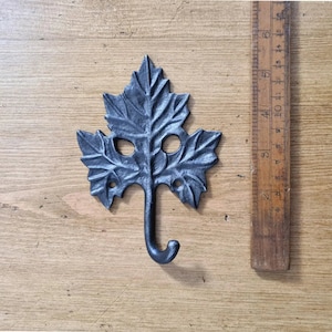 May include: A black cast iron leaf-shaped hook with a single hook at the bottom. The hook is about 5 inches tall and is shown against a wooden background.