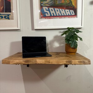 K&ouml;nnte beinhalten: Ein an der Wand montierter Holztisch mit einem Laptop und einer Topfpflanze. Der Tisch ist aus Naturholz mit einer hellbraunen Oberfl&auml;che. Der Laptop ist schwarz und hat eine silberne Tastatur. Die Pflanze ist gr&uuml;n und hat einen gelben Topf.