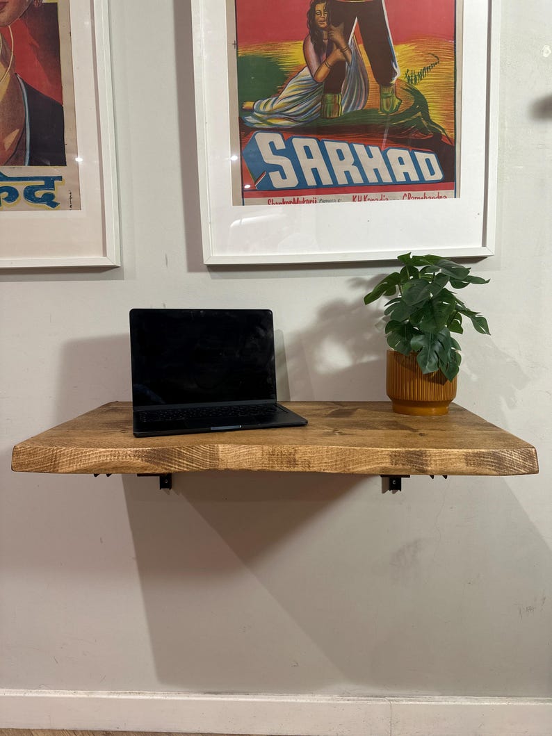 K&ouml;nnte beinhalten: Ein an der Wand montierter Holztisch mit einem Laptop und einer Topfpflanze. Der Tisch ist aus Naturholz mit einer hellbraunen Oberfl&auml;che. Der Laptop ist schwarz und hat eine silberne Tastatur. Die Pflanze ist gr&uuml;n und hat einen gelben Topf.