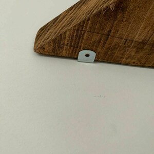 May include: A close-up of a wooden shelf bracket with a metal bracket attached to the bottom. The shelf bracket is stained a dark brown colour.