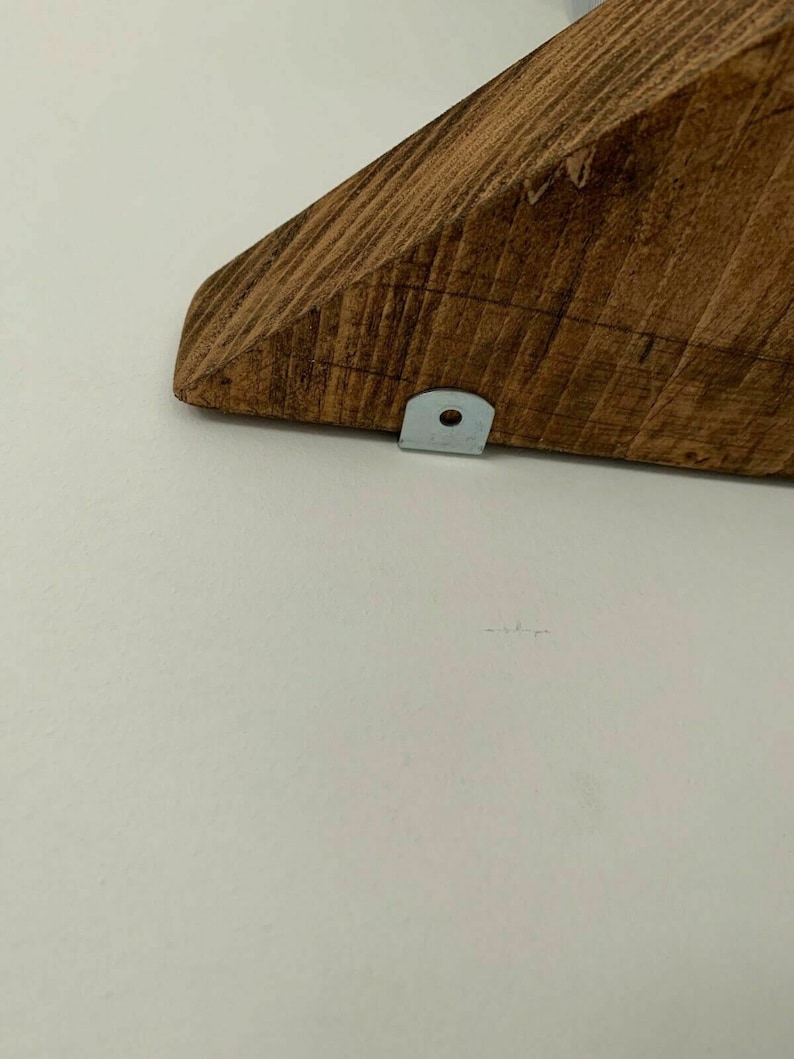 May include: A close-up of a wooden shelf bracket with a metal bracket attached to the bottom. The shelf bracket is stained a dark brown colour.