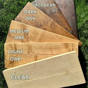 K&ouml;nnte beinhalten: Sechs Holzproben, die in verschiedenen Farben gebeizt sind, von hellster bis dunkelster: Klar, Helles Eichenholz, Mittleres Eichenholz, Dunkles Eichenholz, Jacobean, Nussbaum.