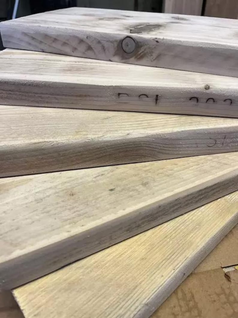 May include: Stack of four unfinished wooden planks, showing the natural grain of the wood. The top plank has a small hole in the center.