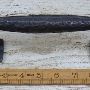 May include: A dark grey, hammered metal handle with a rectangular grip and square mounting plates. The handle is approximately 23 cm long. The mounting plates have four screw holes each. A wooden ruler is in the foreground.