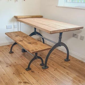 May include: A wooden dining table and bench set. The table has a light brown, rectangular top with a matching bench. Both pieces have dark metal legs. The table is approximately 183 cm long, and the bench is about 122 cm long.